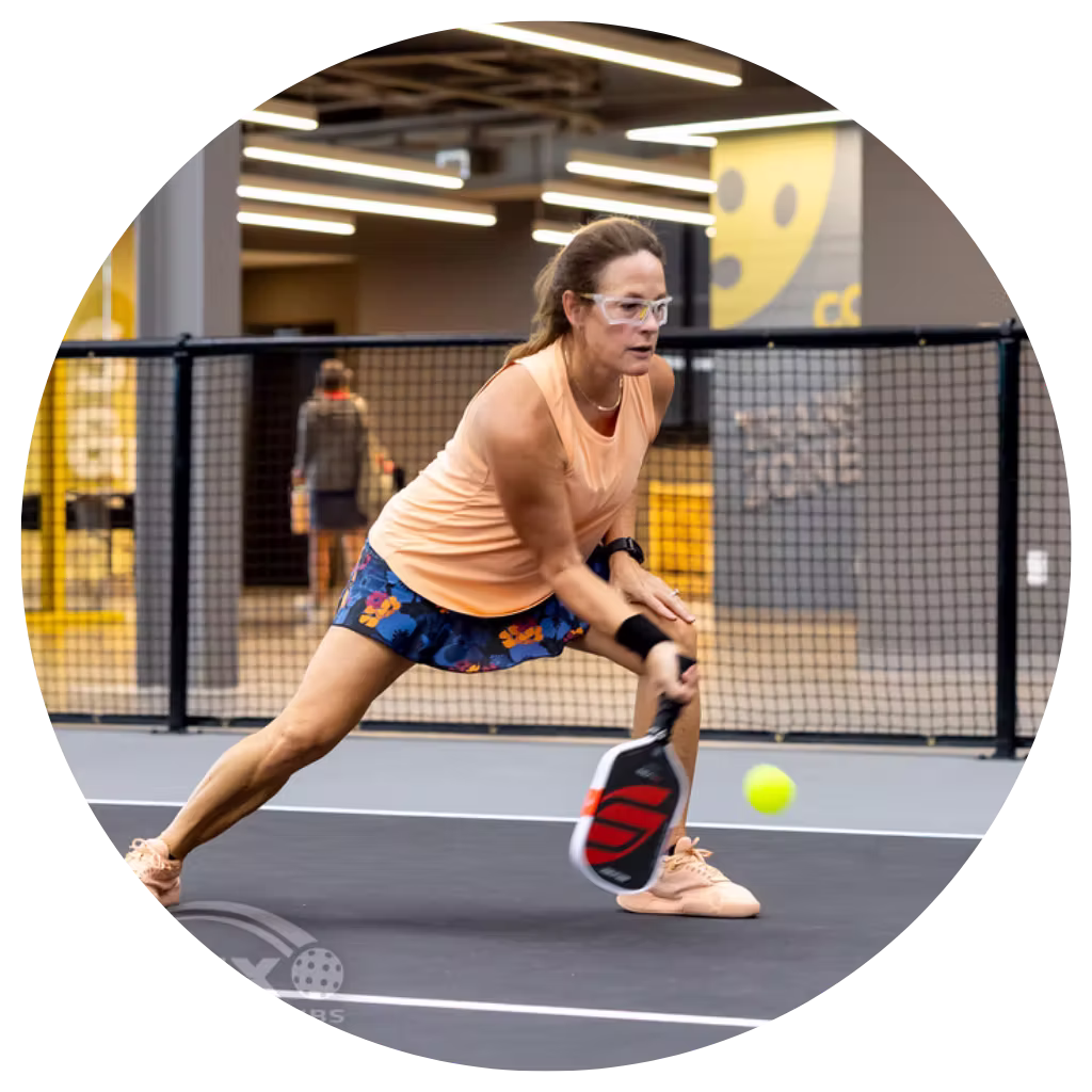 Woman pickleball player making a low paddle return on indoor court at Apex Pickleball Clubs in Cedar Park Texas