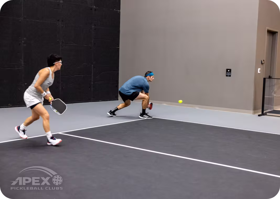 Doubles partners practicing baseline returns during pickleball lesson at Apex Pickleball Clubs indoor courts in Cedar Park Texas